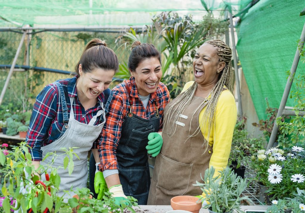 Happy multiracial gardeners having fun working in plants and flowers garden shop